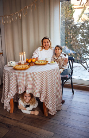 Family enjoys a cozy gathering at a table filled with treats and candles, creating a warm atmosphere during winter, with children playing and laughter filling the roomの写真素材