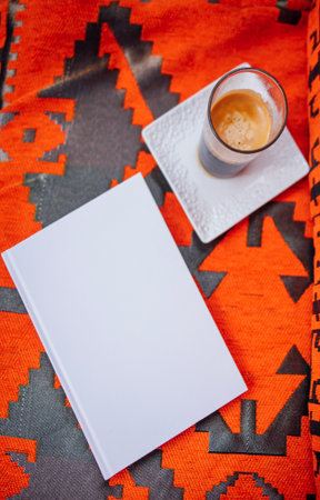 Blank notebook rests on colorful fabric next to a cup of coffee on a plate, inviting creativity and relaxation in a warm, cozy settingの写真素材