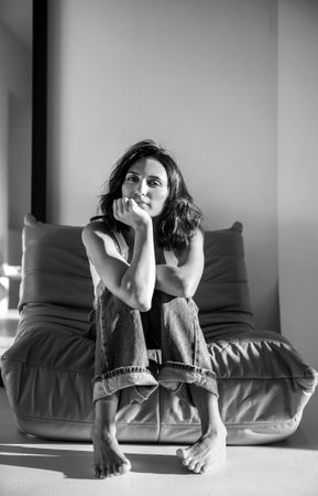 Female figure seated on contemporary couch, deep in thought, with soft light enhancing her expression, evoking a sense of calm and introspection in a minimalist spaceの写真素材