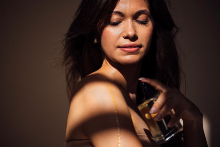 Female figure with long hair, holding perfume bottle, is captured in soft light and shadows,...