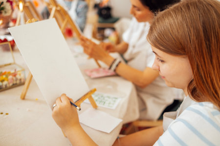 Female artist is focused on painting on a blank canvas in a vibrant workshop, with other participants engaged in creative activities and artistic explorationの写真素材