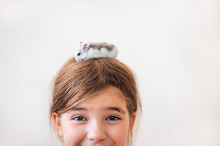 Happy young girl with brown hair, a small hamster on her head, radiating joy and warmth, capturing a delightful moment of companionship and innocenceの写真素材