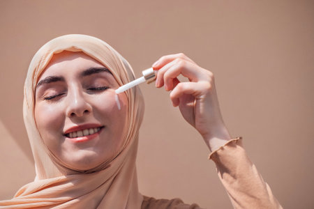 Young woman with hijab is applying serum to her face, highlighting her skincare routine, with soft...