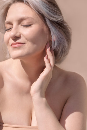 Female with silver hair is softly touching her face, basking in sunlight, radiating tranquility and natural beauty in a serene, minimalistic settingの写真素材