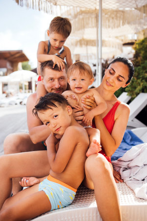Family relaxing at a resort, with children playfully interacting with parents, surrounded by sun loungers and a vibrant pool area, showcasing joyful summer momentsの写真素材