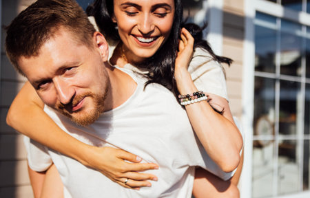 Playful couple sharing a joyful moment outdoors, with one partner on the back of the husband,...