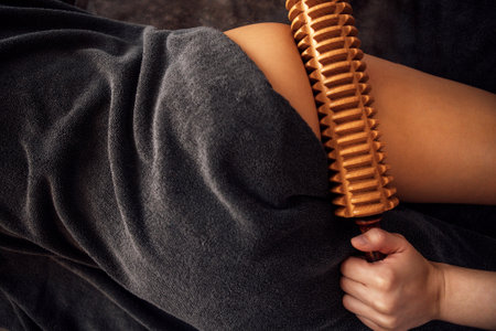 Woman enjoys a soothing massage with a wooden roller on her back, wrapped in a cozy gray towel, creating a serene atmosphere for relaxation and wellnessの写真素材