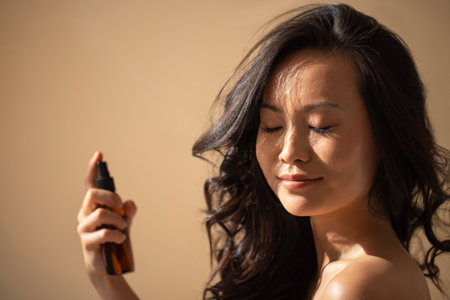 Female applying facial mist with closed eyes, highlighting her glowing skin and natural beauty, surrounded by soft light and a neutral backdrop, enhancing skincare ritualの写真素材