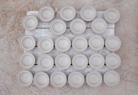 Gray ceramic bowls are neatly arranged in a grid on a wooden pallet, set against a textured concrete...