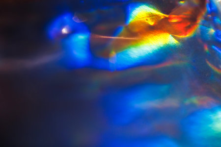 Colorful light reflections create a vibrant pattern on a dark surface, featuring a blend of blue,...
