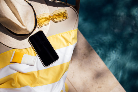 Poolside lounge chair displays summer essentials including a smartphone, sunscreen, sunglasses, and...