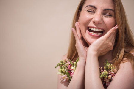 Happy woman with flowers, smiling widely, showcasing joy and positivity, set against a soft background, creating an uplifting and vibrant atmosphere of celebrationの写真素材