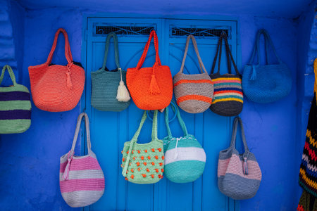 Woven bags in multiple colors and patterns hang on a blue wall, featuring a vibrant blue door as a...