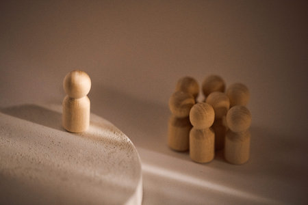 Wooden figure stands on a circular base, facing a cluster of smaller wooden figures grouped together on a plain surfaceの写真素材