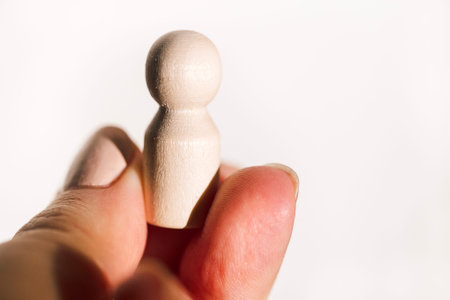 Hand is grasping a small wooden figurine with a smooth finish, positioned against a bright background that emphasizes the object shape and textureの写真素材
