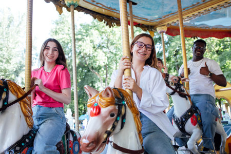 Young friends are riding a carousel on vibrant horses, sharing laughter and smiles, creating a joyful atmosphere of friendship and amusement park excitementの写真素材