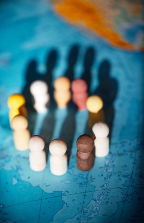 Wooden figurines of different colors are positioned in a circle on a world map, with their shadows...