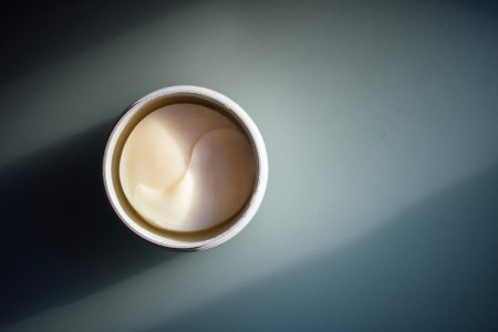Round container filled with creamy white lotion placed on a smooth surface, highlighting the...
