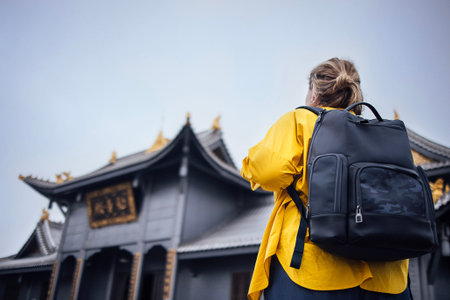 Woman in yellow jacket by Temples and monuments complex on the Golden Summit of Emeishan mountain,...