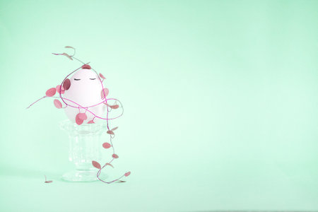 Pink decorative plant with a smiling face rests on a glass pedestal, surrounded by trailing vines,...