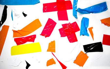 Torn pieces of adhesive tape in multiple colors are scattered across a white surface, creating a dynamic and colorful composition