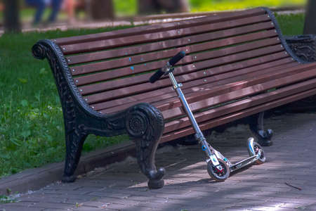 Scooter around brown bench in summer parkの写真素材
