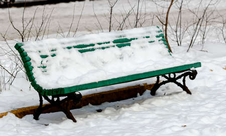Nice snow-covered bench in winter park at dayの写真素材