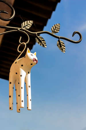 Wooden figurine of cat hanging at entrance to house on blue sky backgroundの写真素材