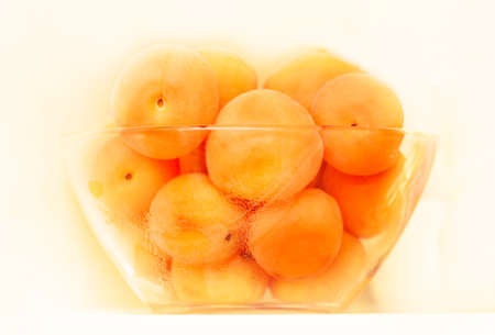 Ripe apricots in glass bowl on light backgroundの写真素材