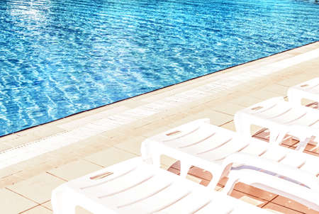 White plastic sunbeds at pool with blue water at sunny morning