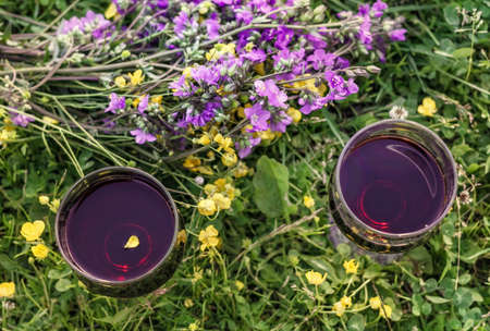 Two glasses of red wine in meadow flowers at sunny cloudy dayの写真素材