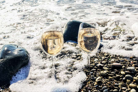 Two glasses of white wine in sea waves at sunny weatherの写真素材