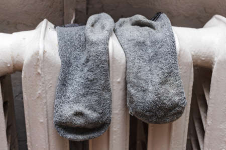 Old grey socks to dry on battery in room at dayの写真素材