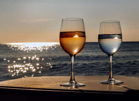 Two glasses of wine at sunset by sunny rays seaの写真素材