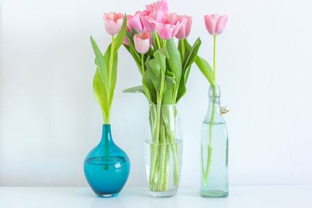 Pink tulips bouquet in glass vase on white background copy space, spring flowers in water on the table, gift for woman, greeting card, freshness and blossomの写真素材