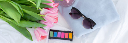 Pink tulips, colorful eye shadow palette, perfume, sunglasses and blue sweater on white background, women make up cosmetics set, female branding, gift for women, fresh flowers bouquet bannerの写真素材
