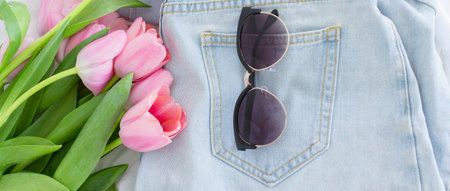 Fashion blog content with flat lay of blue jeans, sunglasses and pink tulips bouquet, minimalistic...