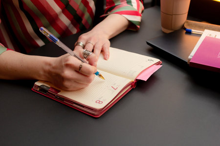 Woman writing in notebook at the table, silver rings on women fingers, girl taking notes,...