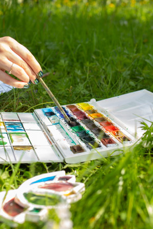 Brush in hand and watercolor palette, woman drawing and painting on plain air in the summer park on sunny day, creative hoppy for girlsの写真素材