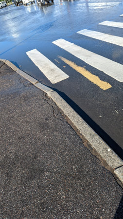 Asphalt road after the rain and crosswalk with reflections, vertical photo of wet empty street