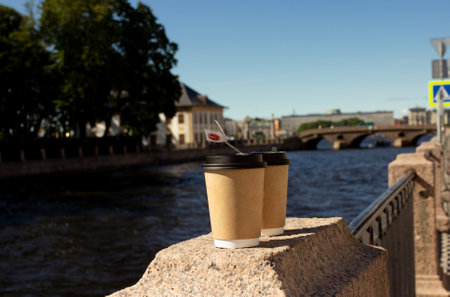 Two coffee and tea cups standing outdoor on stone embankment near the river in the city, morning routine, take away coffee, coffee to go, tea cups on the streetの写真素材