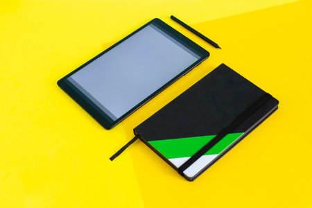 Home office flat lay with tablet and black notebook on yellow background