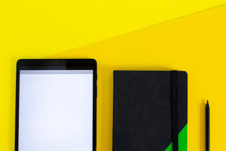 Home office flat lay with tablet and black notebook on yellow backgroundの写真素材