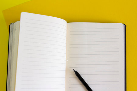 Open blank notebook and black pencil on yellow and blue background, white pages close up, school and...