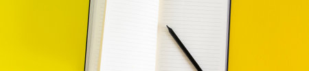 Open blank notebook and black pencil on yellow and blue background, white pages close up, school and work supply on desk, copy space empty book for notes and writing bannerの写真素材