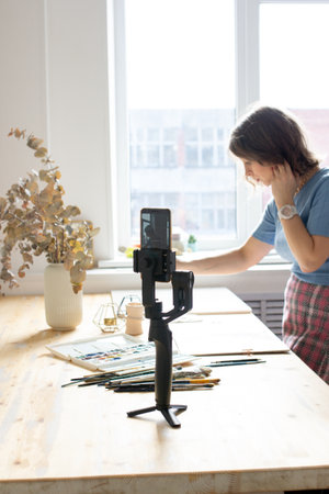 Young woman painting a picture with watercolor at wooden table, aquarelle process, girl sitting at...