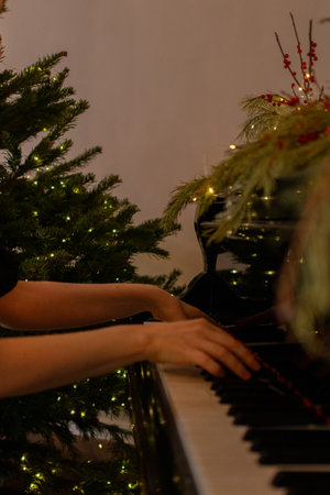 Female musician hand touching white black keys. Woman plays the piano on festive background. Girl in black dress. Vintage Christmas moodの写真素材