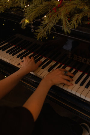 Female musician hand touching white black keys. Woman plays the piano on festive background. Girl in...
