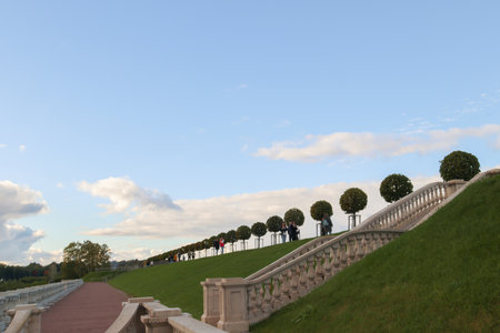 Row of decorative trees spaced along a pathway atop an elevated terrace. People walk along the pathway, contrasting against blue sky and wall below, scenic shotの写真素材
