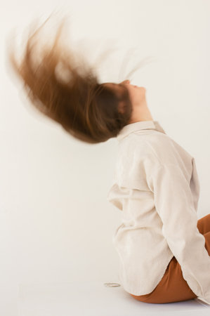 Young woman with long brown hair leans back with closed eyes, enjoying a moment of relaxation. Minimalist portrait with neutral tones, soft lighting and a peaceful atmosphere.の写真素材